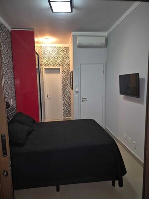Ein Schlafzimmer mit Bett, einer roten Trennwand, einer Tür, einer Klimaanlage und einem Fernseher.