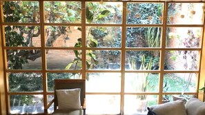 Een kamer met een groot raam bestaande uit meerdere ruitjes, met uitzicht op een tuin met verschillende planten en een bakstenen muur.