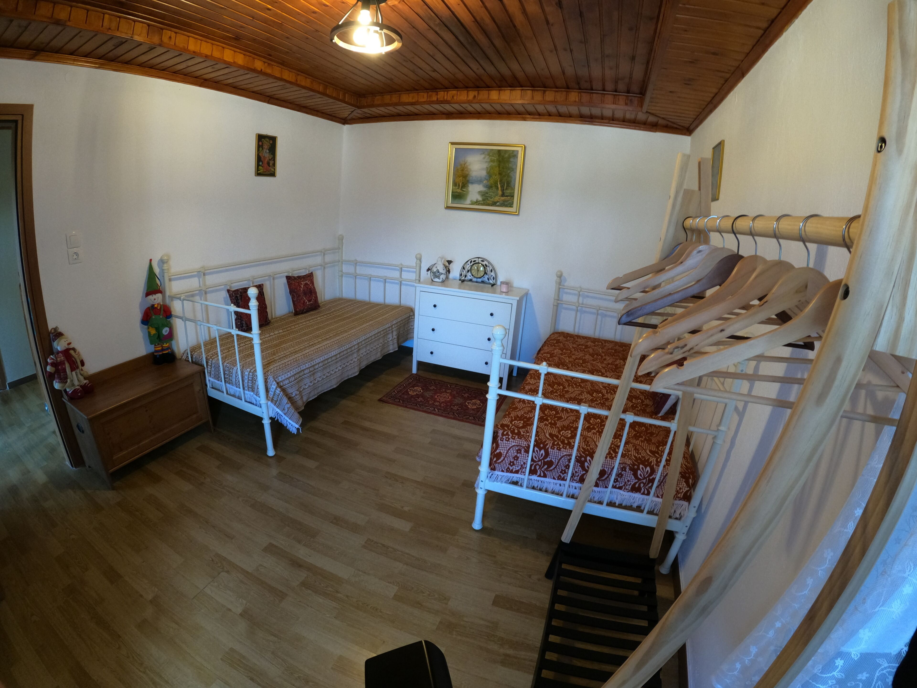 Een kamer met twee bedden, een dressoir, een houten plafond en een schilderij aan de muur.