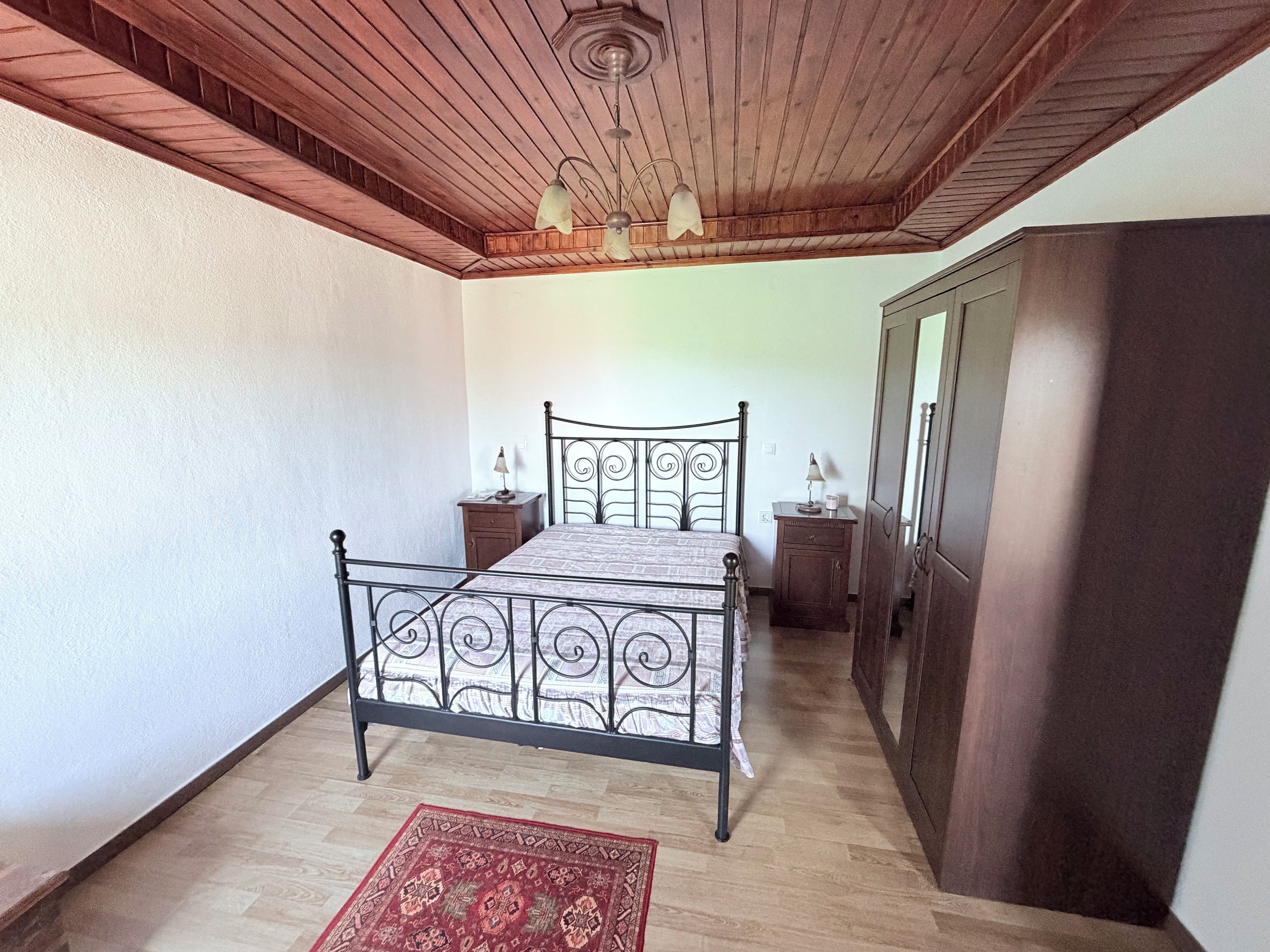 Une chambre à coucher avec un lit en métal, un plafond en bois et un petit tapis.