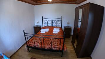 A bedroom with a bed, wooden ceiling, two bedside tables, a wardrobe, and a patterned rug.