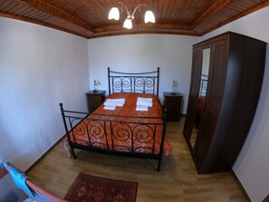 A bedroom with a bed, wooden ceiling, two bedside tables, a wardrobe, and a patterned rug. - PIALEIA  (Pyli)