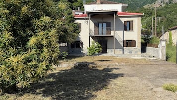 Un edificio de dos pisos con techo de tejas rojas, un pequeño balcón y un muro de piedra.