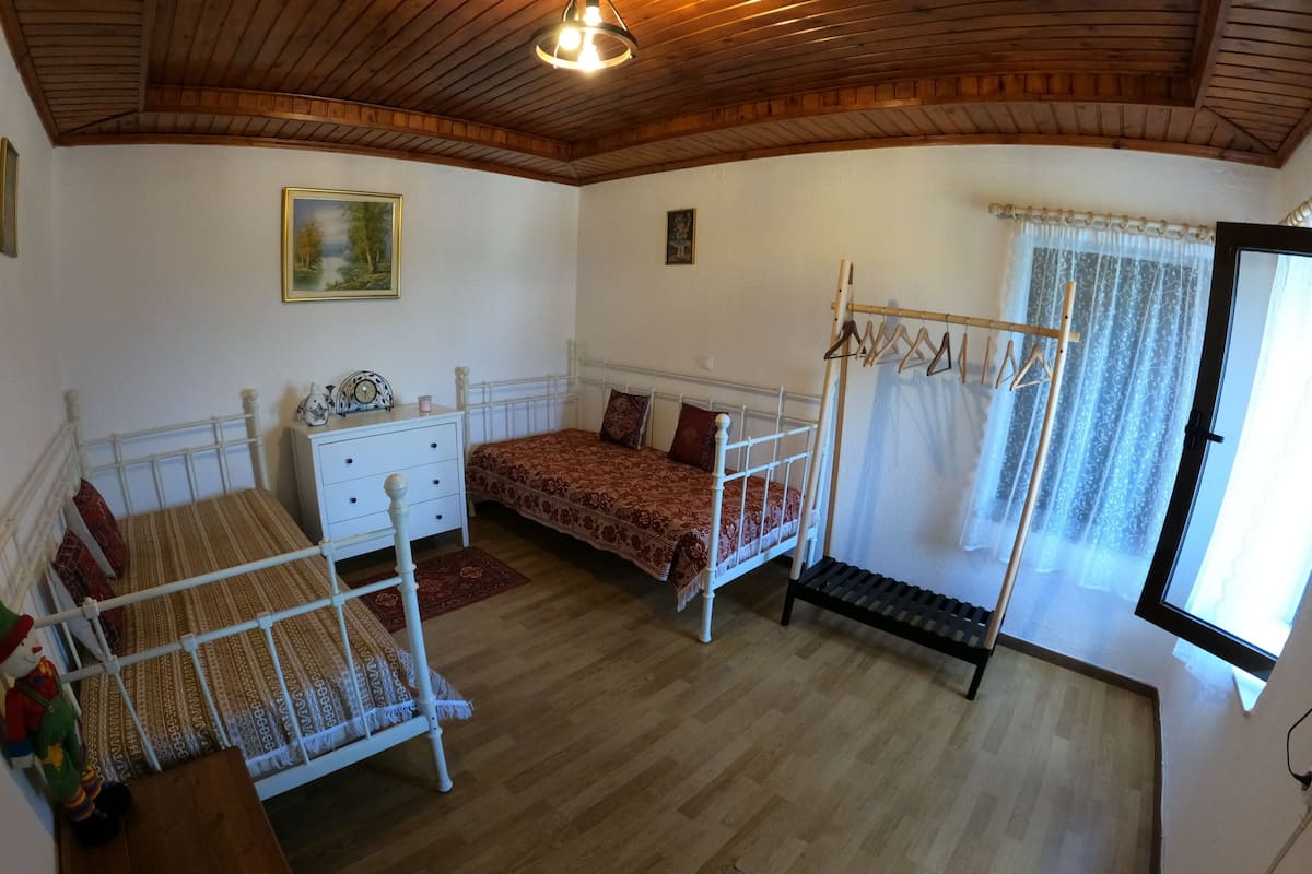 Une pièce avec un plafond en bois, un lit recouvert d’une couvre-lit à motifs, une commode, un banc et une fenêtre avec des rideaux.