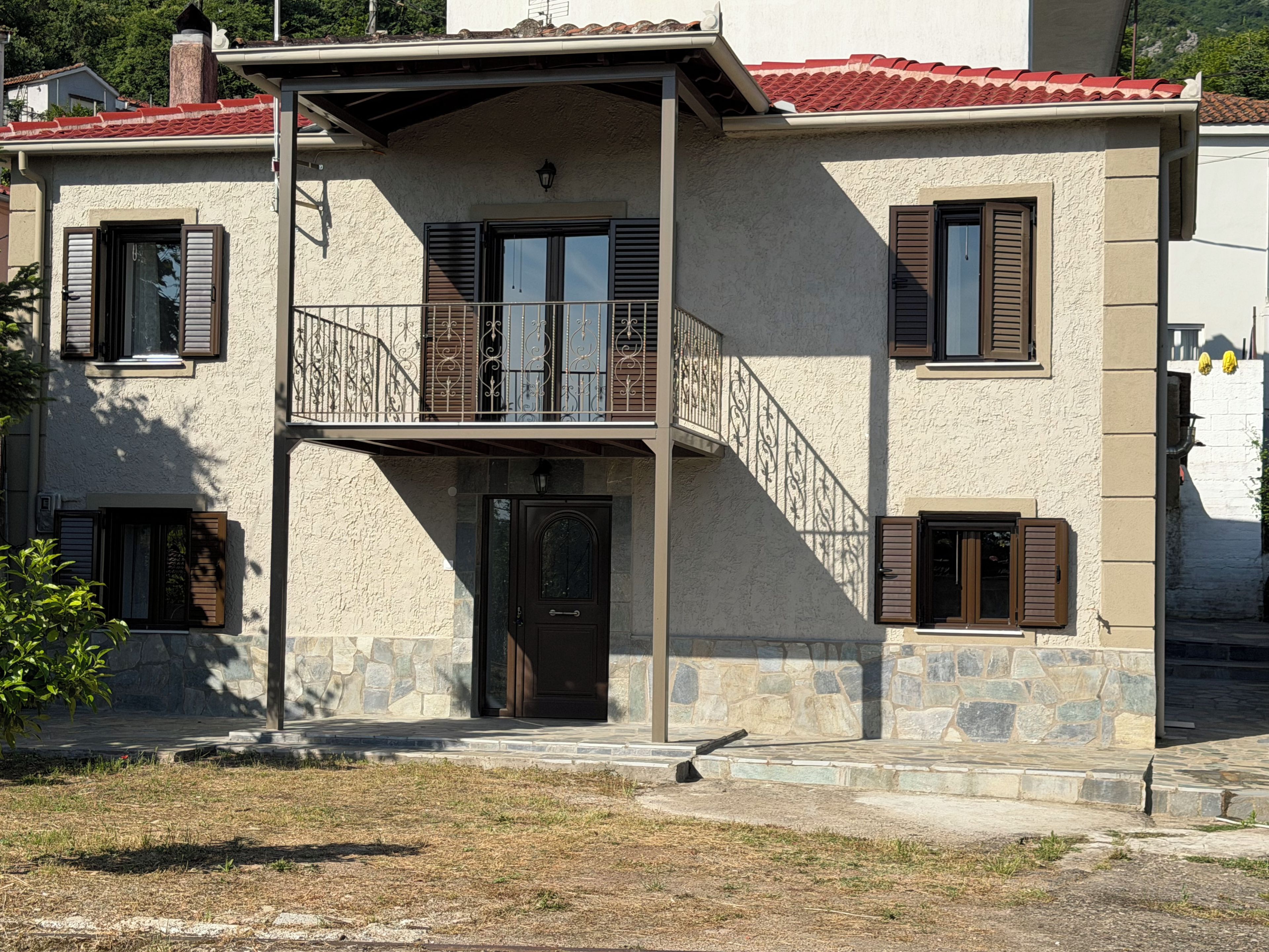 A two-story building with a stone facade, a balcony with metal railings, and a red-tiled roof.
