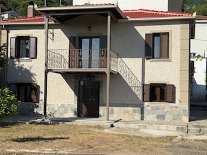 A two-story building with a stone facade, a balcony with metal railings, and a red-tiled roof. - PIALEIA (Pyli)