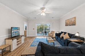 A living room with a dark blue sofa, a coffee table, a TV, and a ceiling fan. - Coastal Retreat at Magnolia Pointe | Golf & Lake Views (Myrtle Beach)