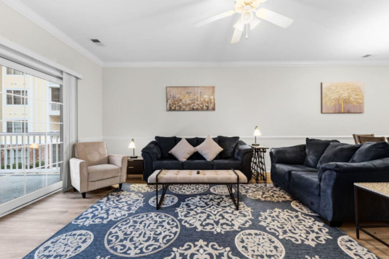 A living room with a sofa, armchair, and ottoman, a patterned rug, and a ceiling fan.