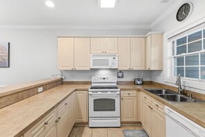 A kitchen with light wooden cabinets, a microwave, a stove, a toaster, and a dishwasher. - Coastal Retreat at Magnolia Pointe | Golf & Lake Views (Myrtle Beach)