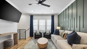 A modern living room with a sofa, two armchairs, a coffee table, a TV, and a ceiling fan. - Curated West Nash Escape | 10 Min to Broadway (Nashville)
