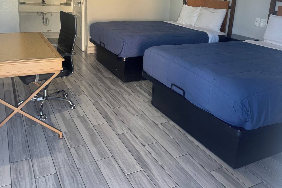 A hotel room with two beds, a desk, and a chair.