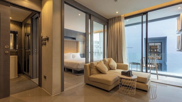Een moderne hotelkamer met een bank, een klein rond tafeltje, een bed en uitzicht op de stad door grote ramen.