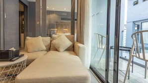 Een moderne hotelkamer met een bank, een klein tafeltje met een afstandsbediening en een glazen deur naar een balkon.