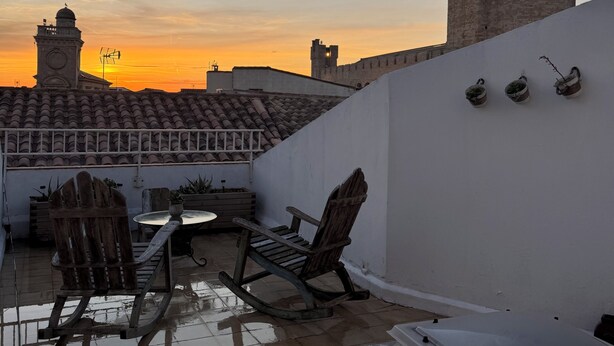 A rooftop terrace with a view of a historic tower, a white wall with potted plants, and a tiled floor. - Charming sea view apartment "Maison Leya (Saintes-Maries-de-la-Mer)