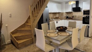 A modern kitchen with white cabinets, a wooden staircase, a dining area with a table and chairs, and a built-in oven. - Charming sea view apartment "Maison Leya (Saintes-Maries-de-la-Mer)