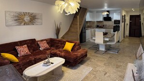 A modern living room with a brown sofa, a coffee table, and a dining area with a white table and chairs. - Charming sea view apartment "Maison Leya (Saintes-Maries-de-la-Mer)