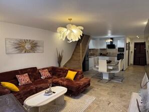 Ein modernes Wohnzimmer mit einem braunen Sofa, einem Couchtisch und einem Essbereich mit weißem Tisch und Stühlen.