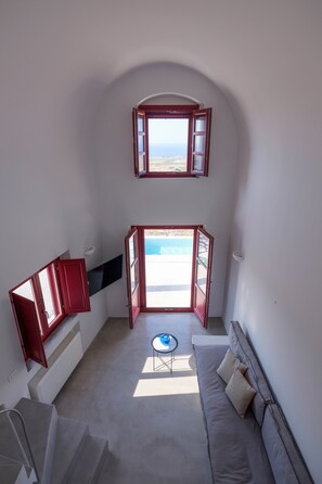 A room with a staircase, a sofa, a small table, and a view of the sea through open doors. - Deluxe Villa with Plunge Pool in Oia (Oia)