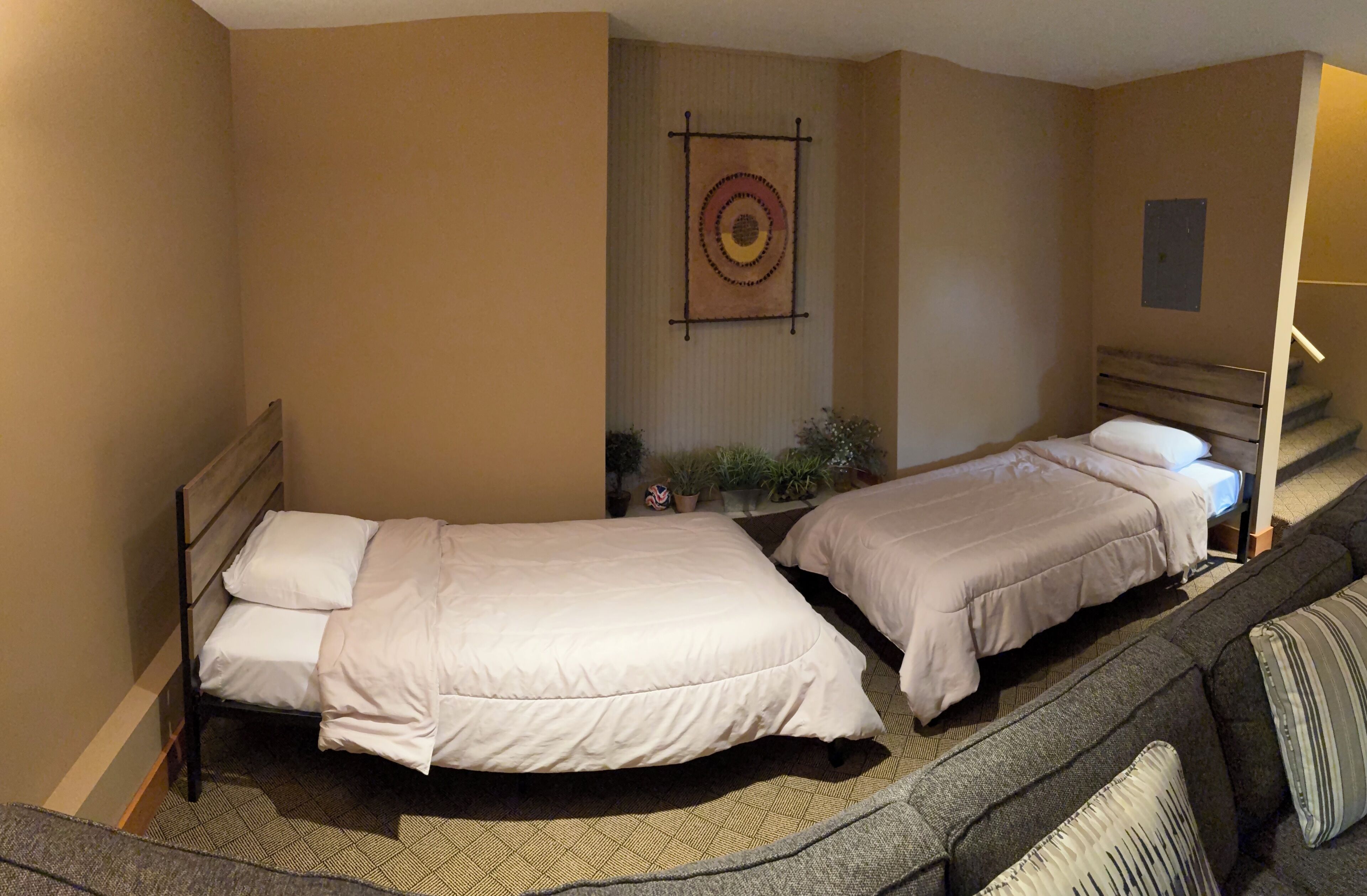 Habitación de hotel con dos camas, una escalera, una obra de arte colgada en la pared y una pequeña planta en maceta.