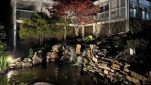 Una casa moderna con un estanque de carpas, una cascada y un árbol de hojas rojas.