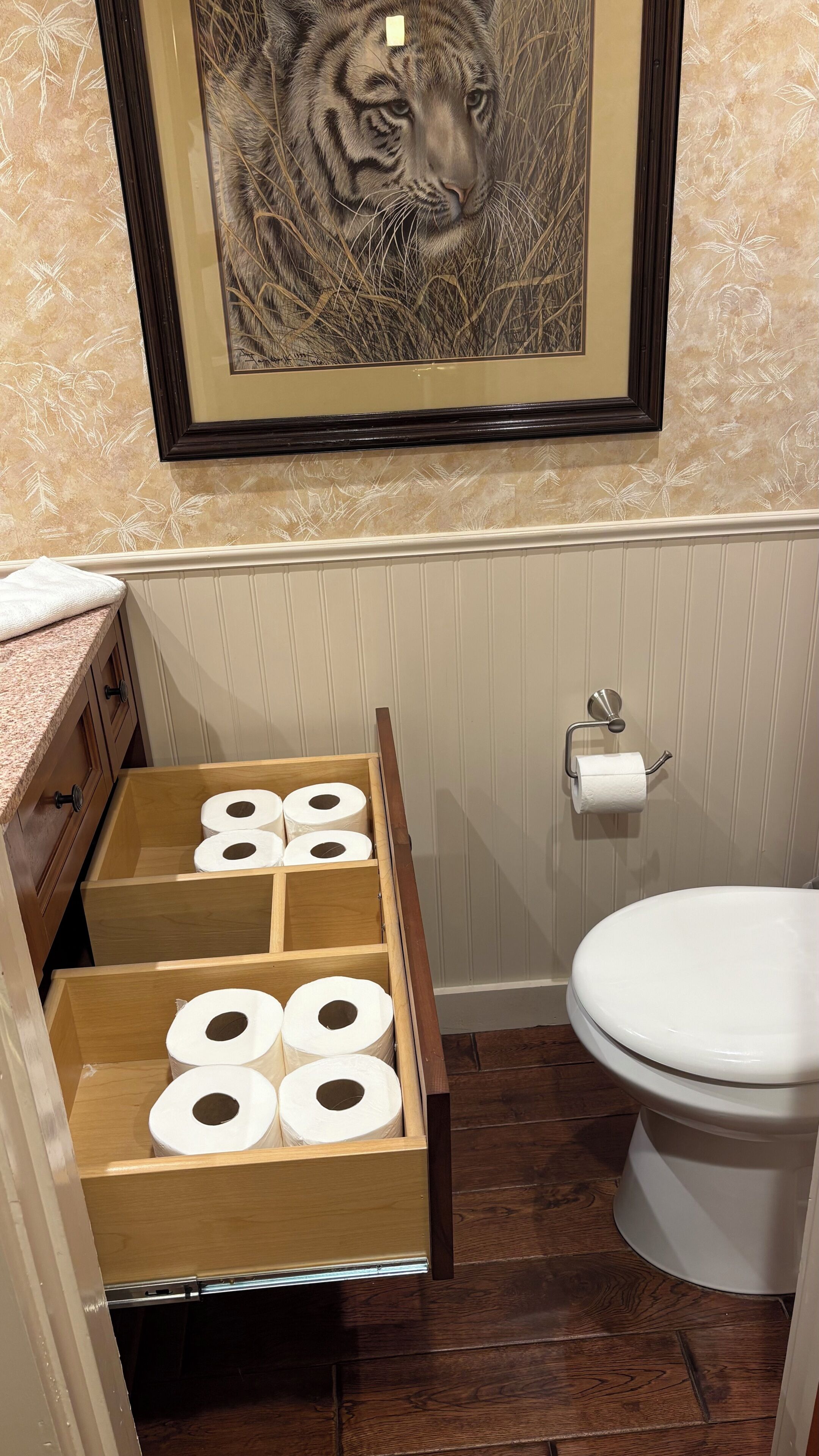 Ein Badezimmer mit Toilette, einer hölzernen Taschentuchbox und einem gerahmten Tiger-Kunstwerk an der Wand.
