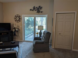 A living room with a TV, a grey sofa, a coffee table, a fireplace, and a door. - Quiet Home Away From Home! (Jackson)
