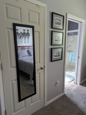 A bedroom with a bed, a door with a mirror, and a bathroom with a shower and glass door.
