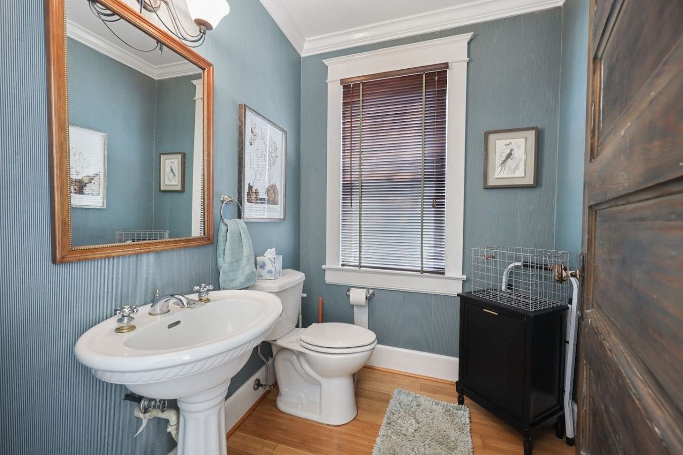 Un baño con lavamanos pedestal, inodoro y ventana con persianas.