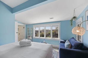 A bedroom with a large bed, a blue sofa, a window with a view, and a hanging plant. - 12 South Sanctuary | Azure Pool & Private Cabana (Nashville)