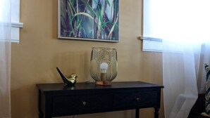 Ett rum med en tavla som hänger på väggen, ett svart konsolbord med en dekorativ fågel och en geometrisk lampa, samt ett eluttag.