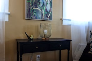 A room with a wall-mounted painting, a black console table with a decorative bird and a geometric lamp, and a power outlet. - 12 South Sanctuary | Azure Pool & Private Cabana (Nashville)