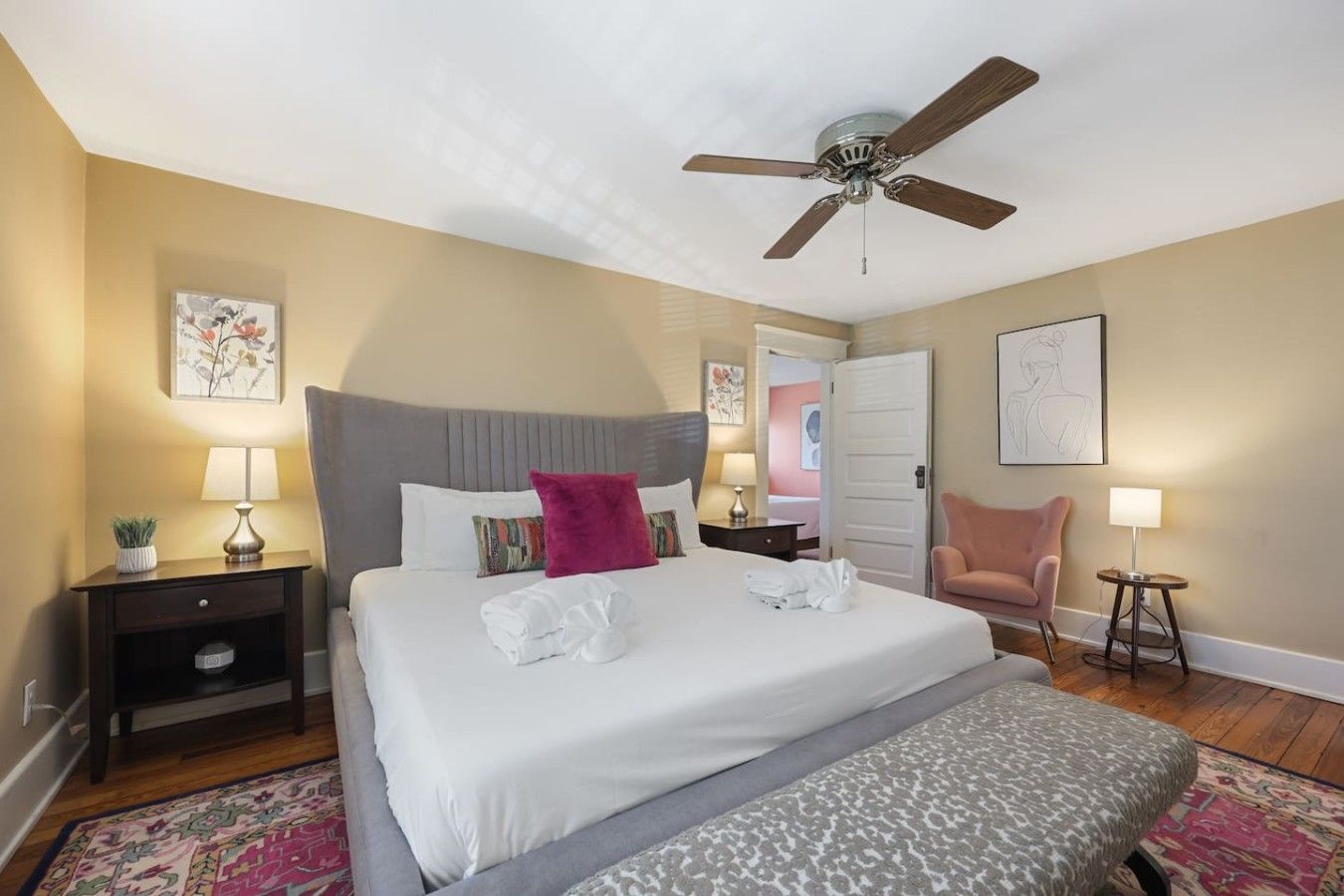 A hotel room with a bed, a ceiling fan, a chair, a bedside table, and a nightstand.