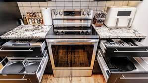 Cozinha com fogão, forno e lava-louças de aço inoxidável, piso de madeira e painel de azulejos.