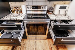 A kitchen with a stainless steel range, oven, and dishwasher, wooden flooring, and a tiled backsplash. - Downtown Two-Level Loft | Private Gym + Parking | Steps From Roger’s Place (Edmonton)