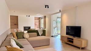Een moderne woonkamer met een hoekbank, een flatscreen-tv op een houten standaard en een inbouwkastenwand.