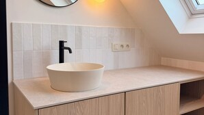 Een moderne badkamer met dakraam, een ronde spiegel, een wit wastafel en houten kastjes.