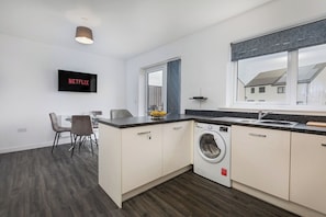 Eine moderne Küche mit Waschmaschine, einem Essbereich mit Stühlen und einem an der Wand befestigten Fernseher.