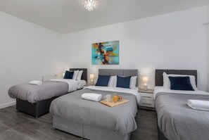 Ein Hotelzimmer mit drei Betten, einer modernen Chandelier und einem farbenfrohen, abstrakten Gemälde an der Wand.