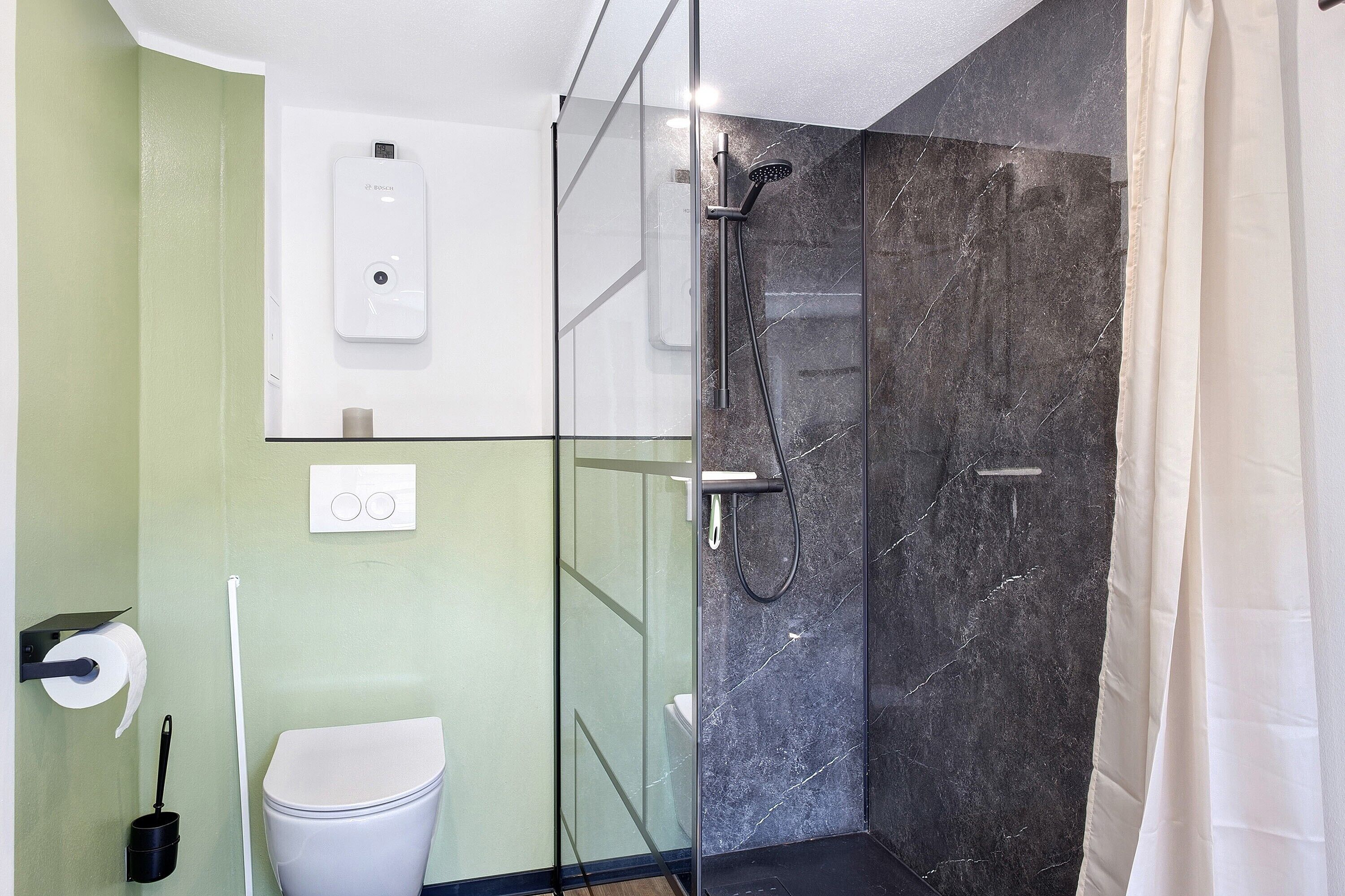 A modern bathroom with a glass-enclosed shower, a toilet, and a hand dryer.