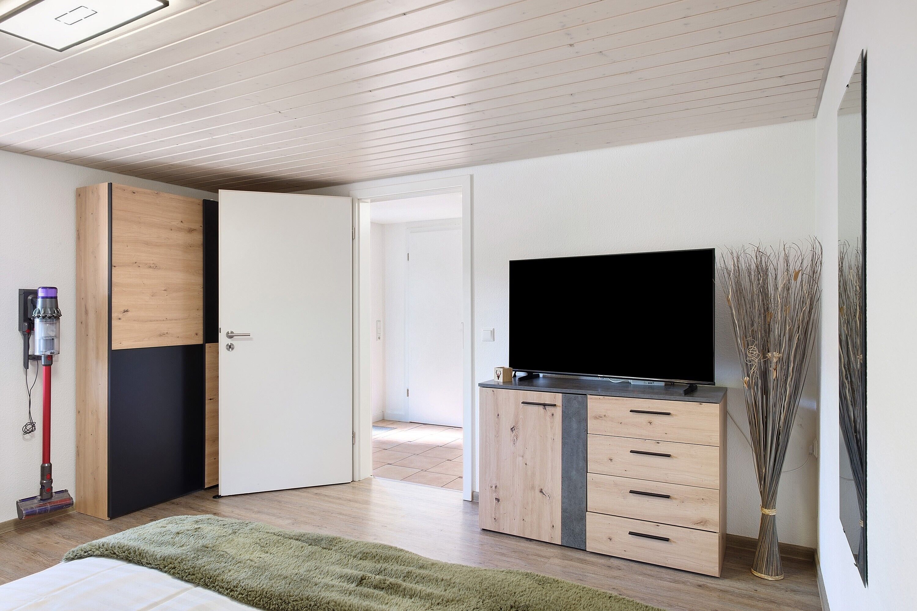 A modern bedroom with a bed, a TV, a wooden cabinet, and a broom.