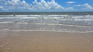 Una playa con olas, cielo despejado y algunas nubes dispersas.