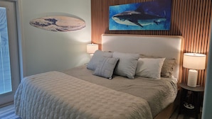 Un dormitorio con cama, almohadas, un cuadro colgado en la pared de un tiburón y pared de paneles de madera.