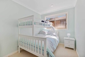 Uma cama de beliche com janela, uma mesa de cabeceira e uma mesinha de apoio em um quarto com paredes em tons claros.