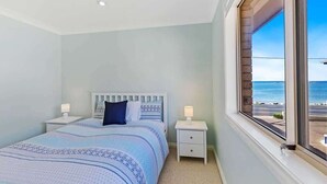 Ein Schlafzimmer mit einem Bett, zwei Nachttischen, einem Fenster mit Meerblick und einer Deckenleuchte.