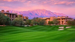 Un parcours de golf avec une chaîne de montagnes en arrière-plan et un bâtiment doté de nombreux balcons.