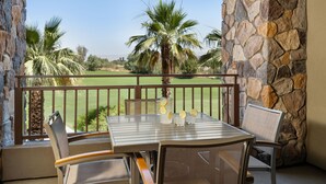Un balcon avec une table, des chaises, une carafe de limonade et une vue sur un terrain de golf.