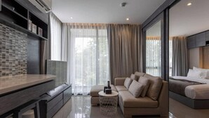 A modern living room with a sofa, a coffee table, a TV, and a bed. - Famous City Gate Walk Beach 4km Patong C142 (Kamala)