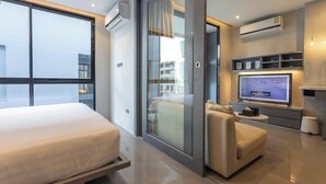 A modern hotel room with a large bed, a seating area with a sofa and armchair, a television, and a balcony with a view. - Famous City Gate Walk Beach 4km Patong C142 (Kamala)