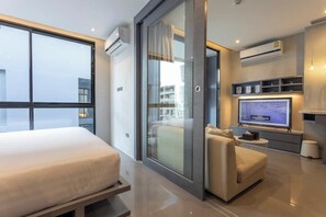A modern hotel room with a large bed, a seating area with a sofa and armchair, a television, and a balcony with a view.