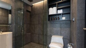 A modern bathroom with a glass-enclosed shower, a toilet, and a shelf with toiletries. - Famous City Gate Walk Beach 4km Patong C142 (Kamala)